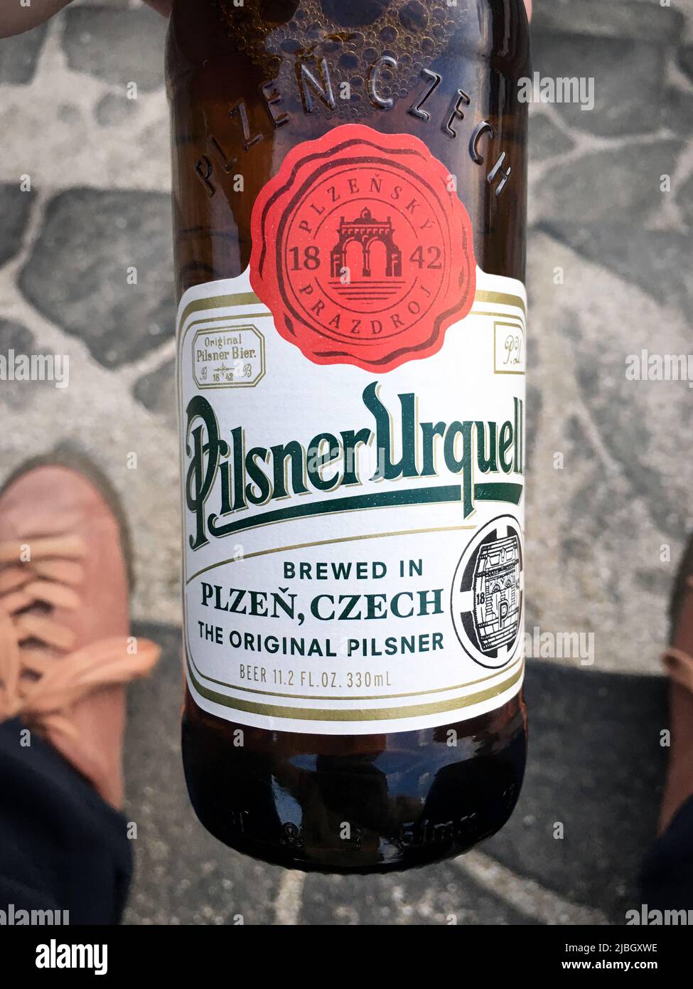 The bottle of Pilsner Urquell, Czech lager brewed by the Pilsner Urquell Brewery in Pilsen, in my hand. It is well known as the first pale lager Stock Photo