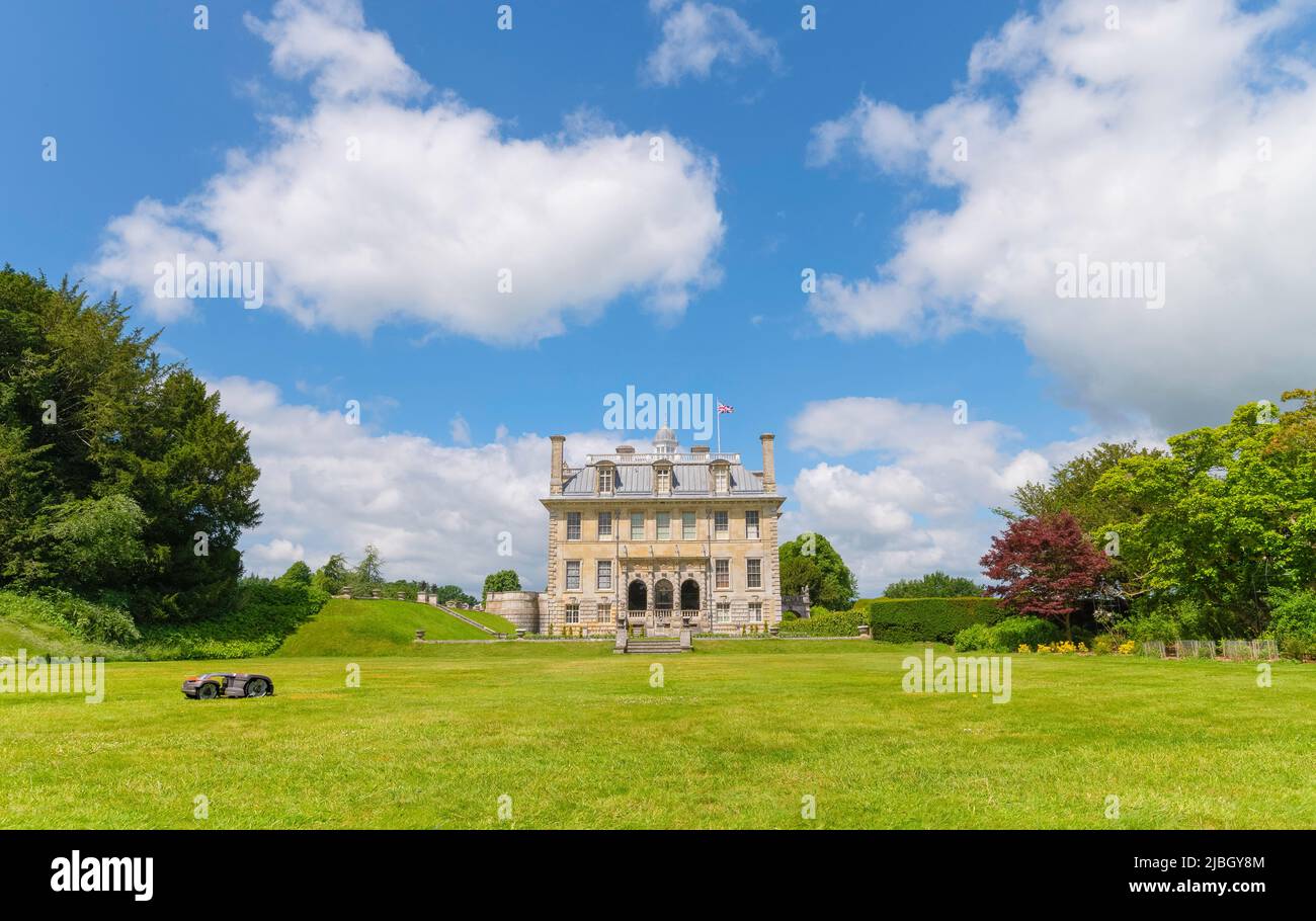 Side of Kingston Lacy Country House with robotic lawnmower by Husqvarna automower cutting the grass on a sunny summers day with Union Jack flag flying Stock Photo