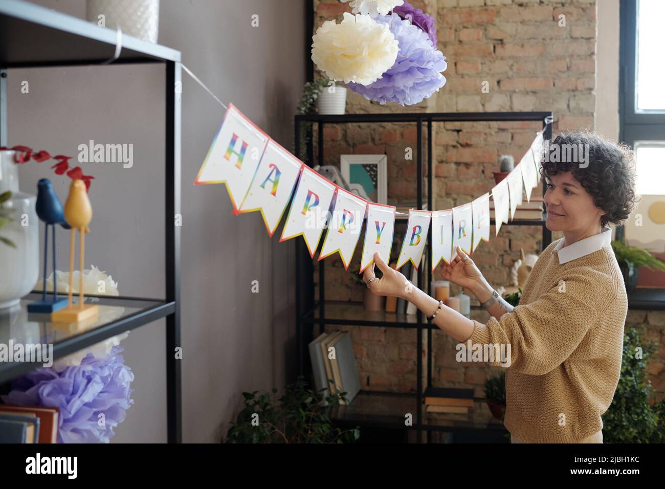 Young woman decorating the room for birthday party hanging Happy