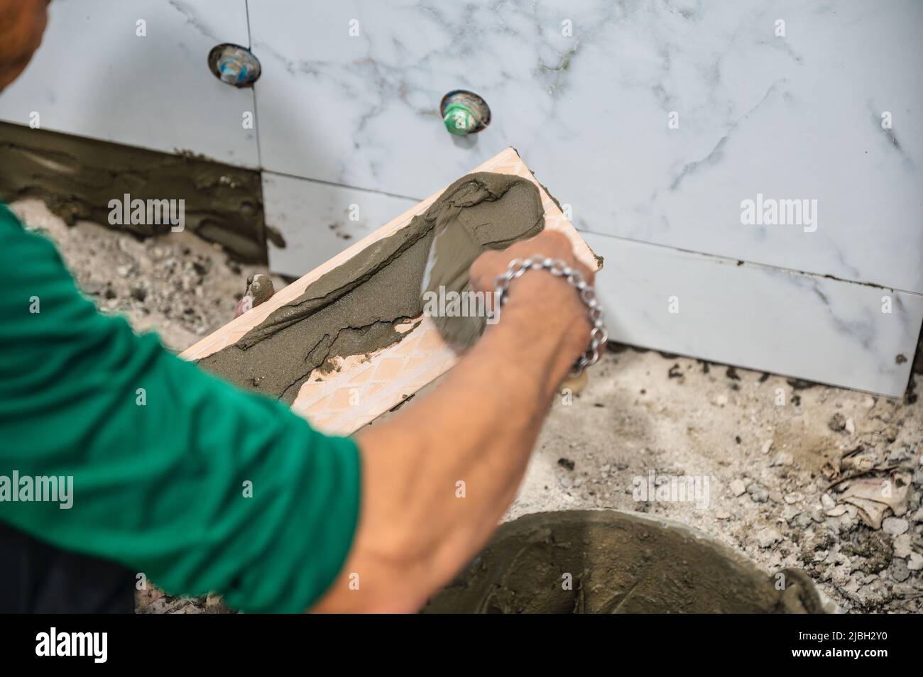 Male tiler using trowel laying marble tile with cement in bathroom. Housing development