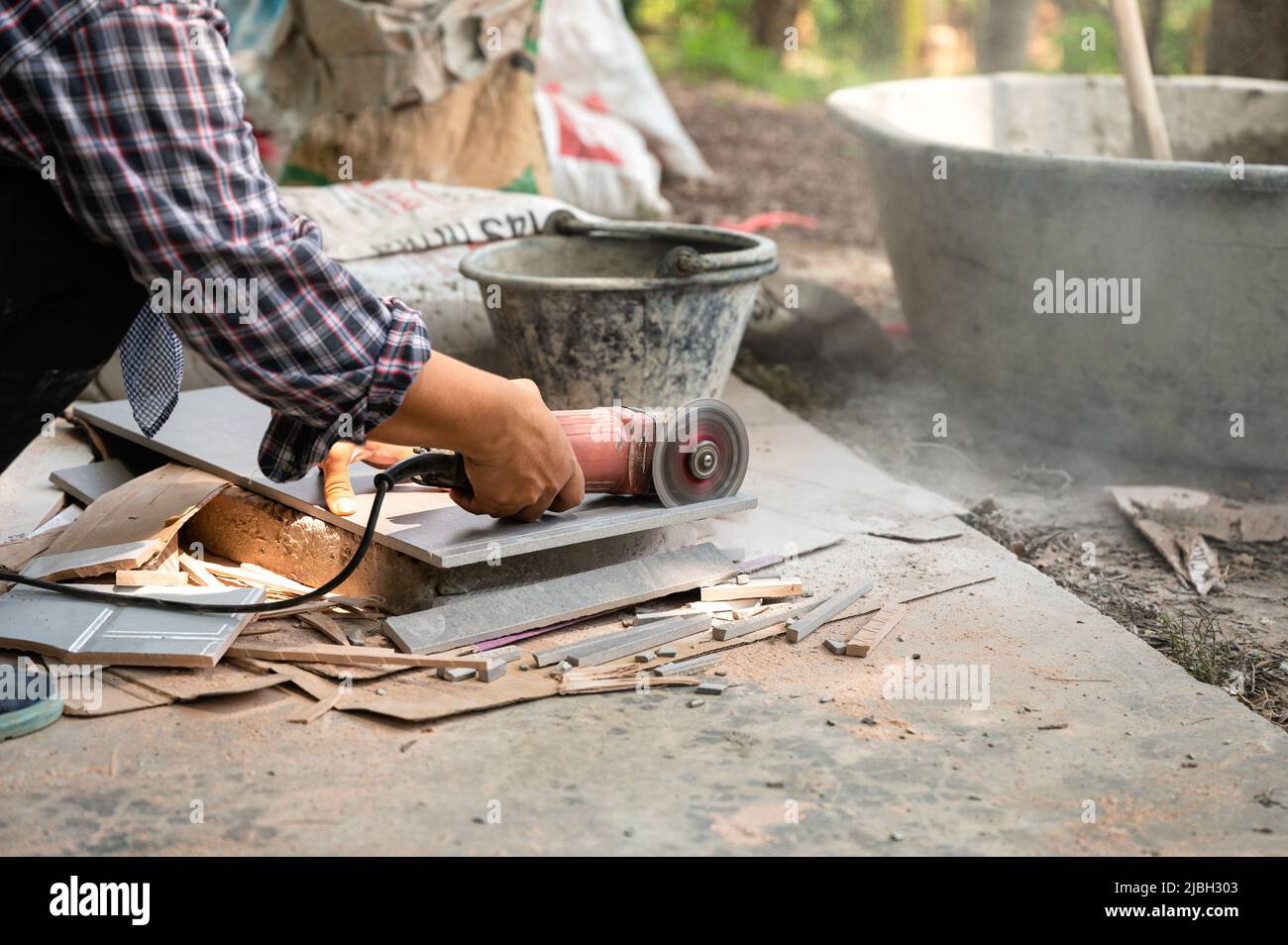 Worker using electric circular saw cutting granite tile in construction site Stock Photo