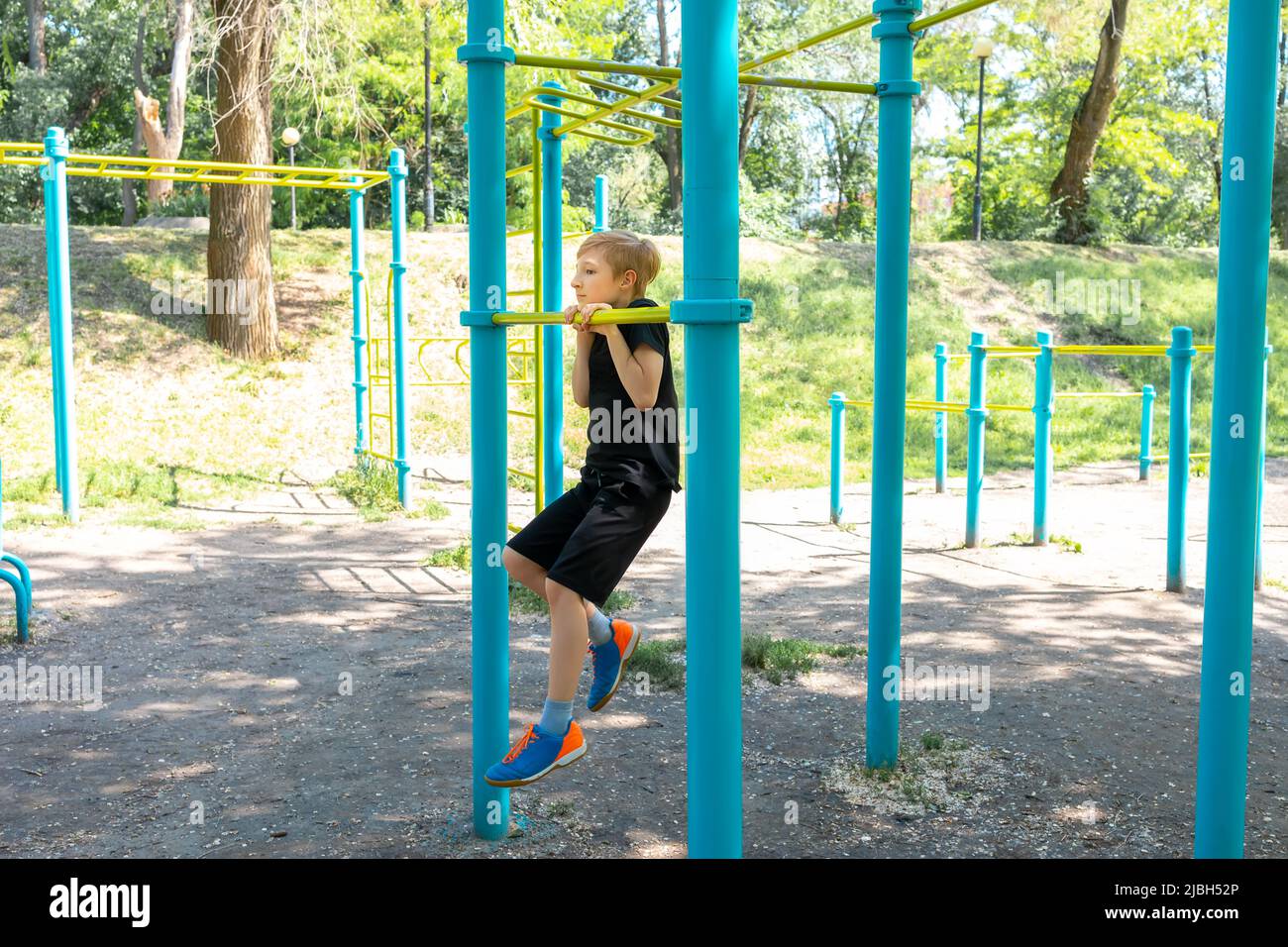 sports boy on the street in the park performs pullups on the crossbar