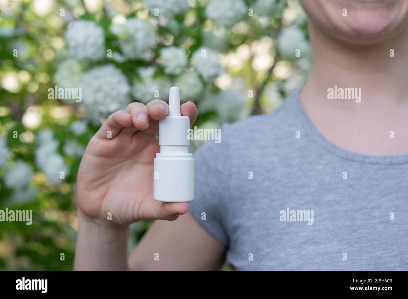 Happy woman demonstrating nasal spray on the background of a blossoming tree.  Stock Photo