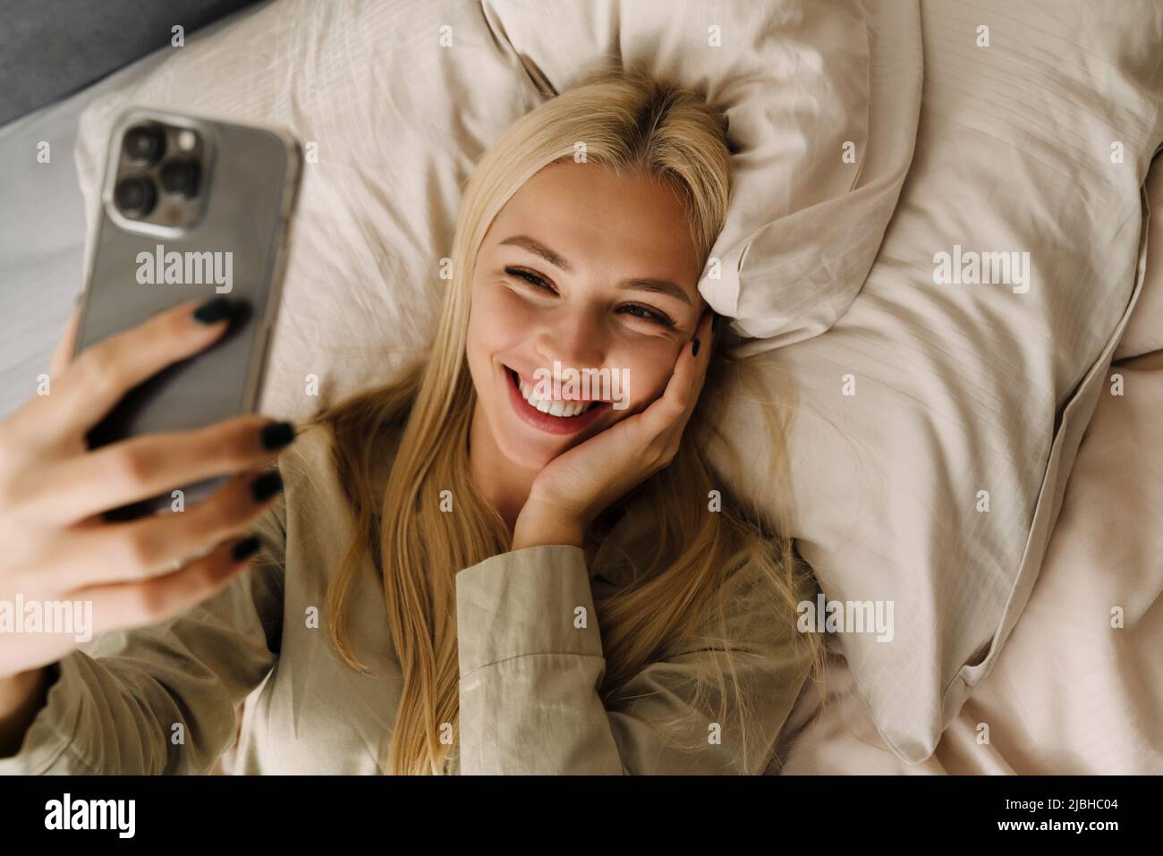 Young blonde woman taking selfie photo while lying in bed after sleep