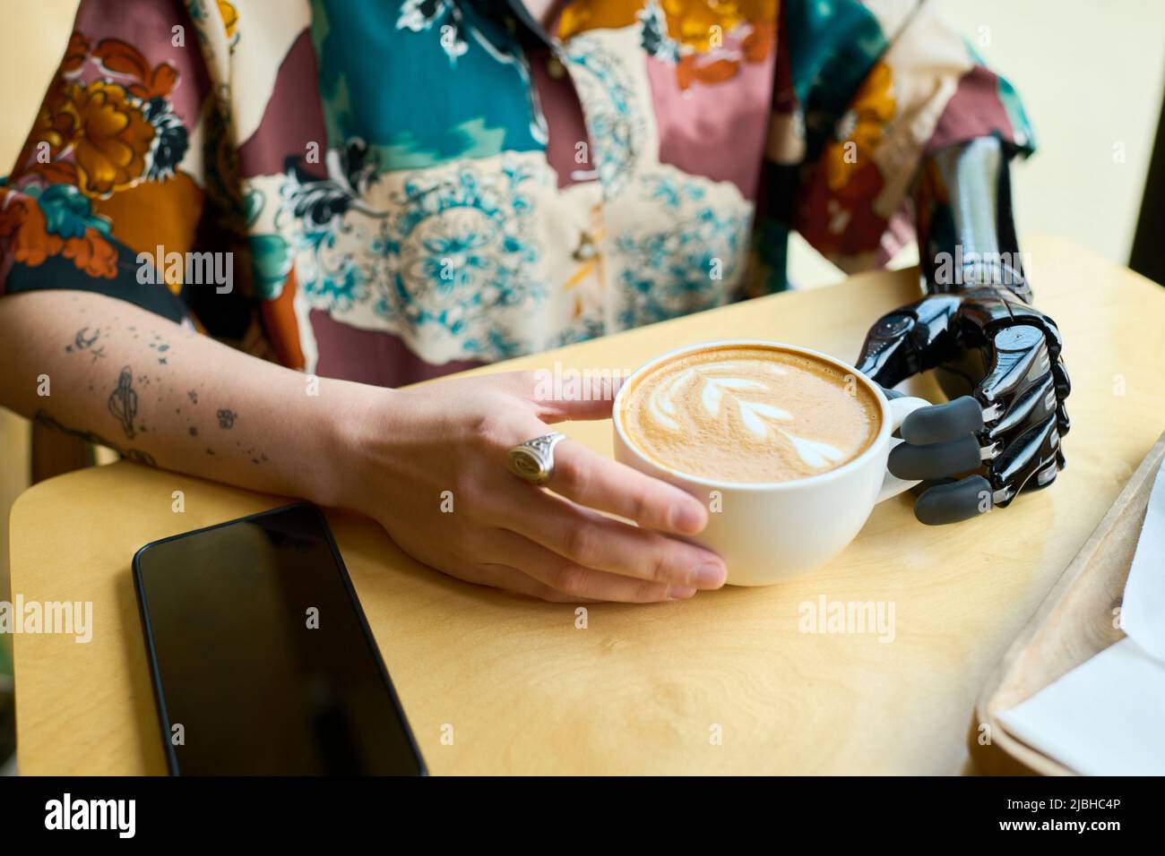 Hands of young woman with partial arm holding cup of cappuccino with fluffy milk foam and creative spiral heart shaped decor Stock Photo