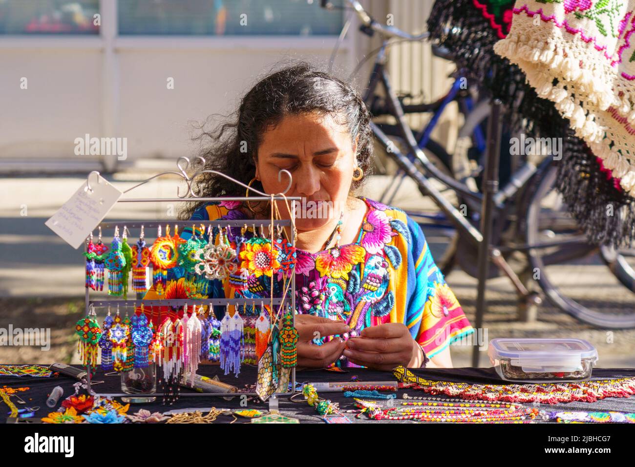 A woman of Latin American ethnicity knits souvenirs in a kiosk that she operates during the Do West Festival Stock Photo