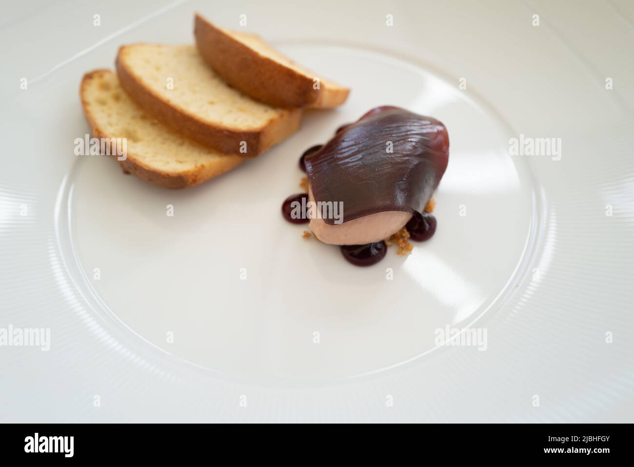 Shallow focus on the jelly on top of a quenelle spoon serving of pate on a plate with toast. Stock Photo