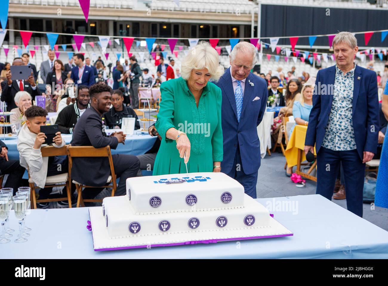 The Prince of Wales looks on as The Duchess of Cornwall cuts a cake on the cricket pitch at the Oval, South London.  In celebration of Her Majesty The Stock Photo