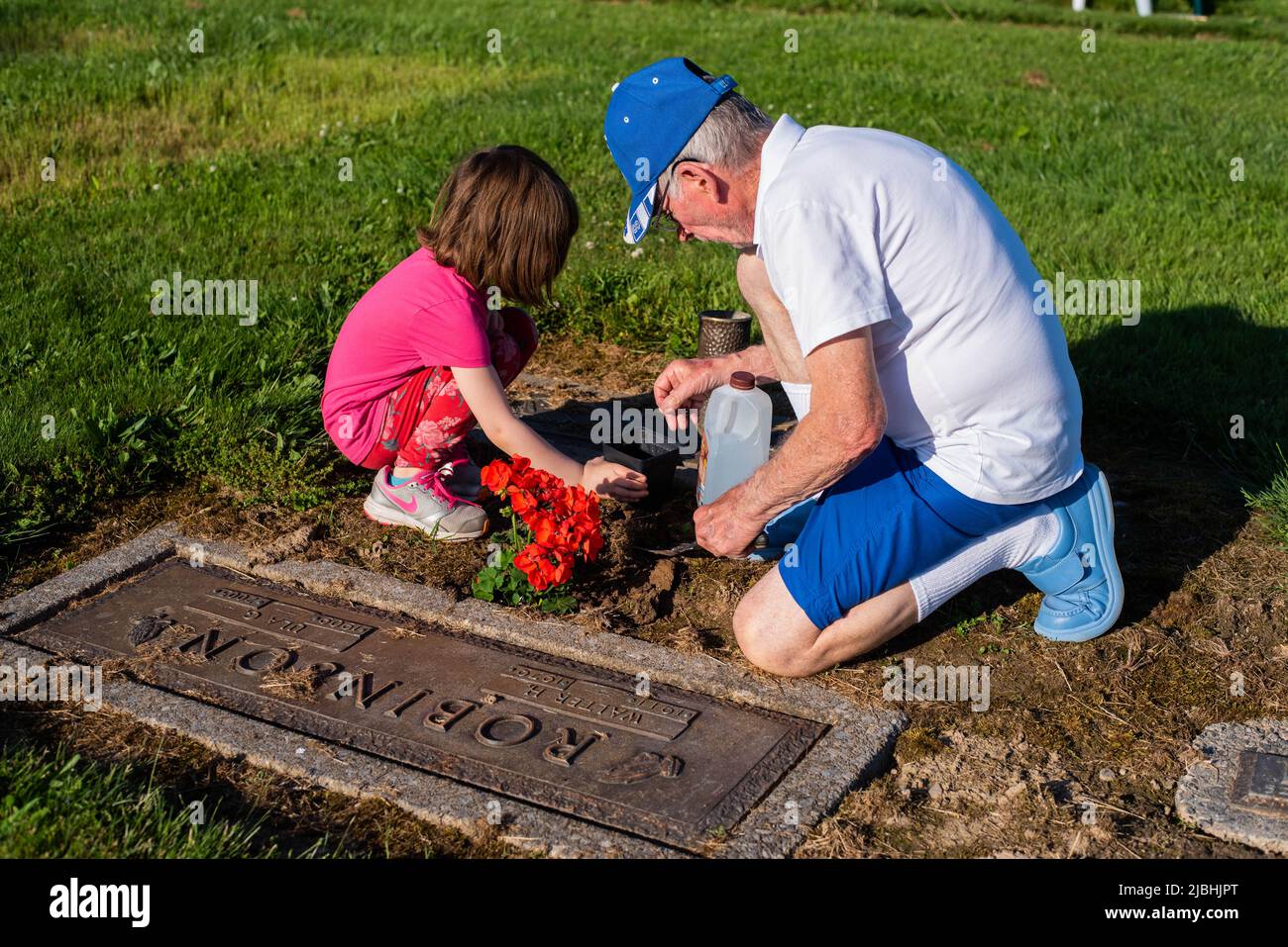 A man and his granddaughter decorate a tombstone at a cemetery on Memorial Day. Stock Photo