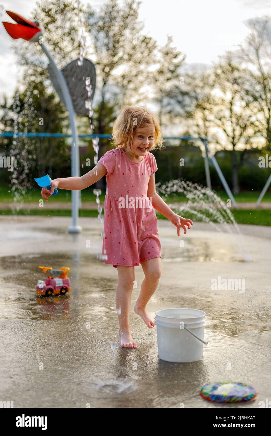 Small happy child playing with outdoor toys at splash pad playground in summer. Water park with fountains for children. Summertime activities for kids Stock Photo