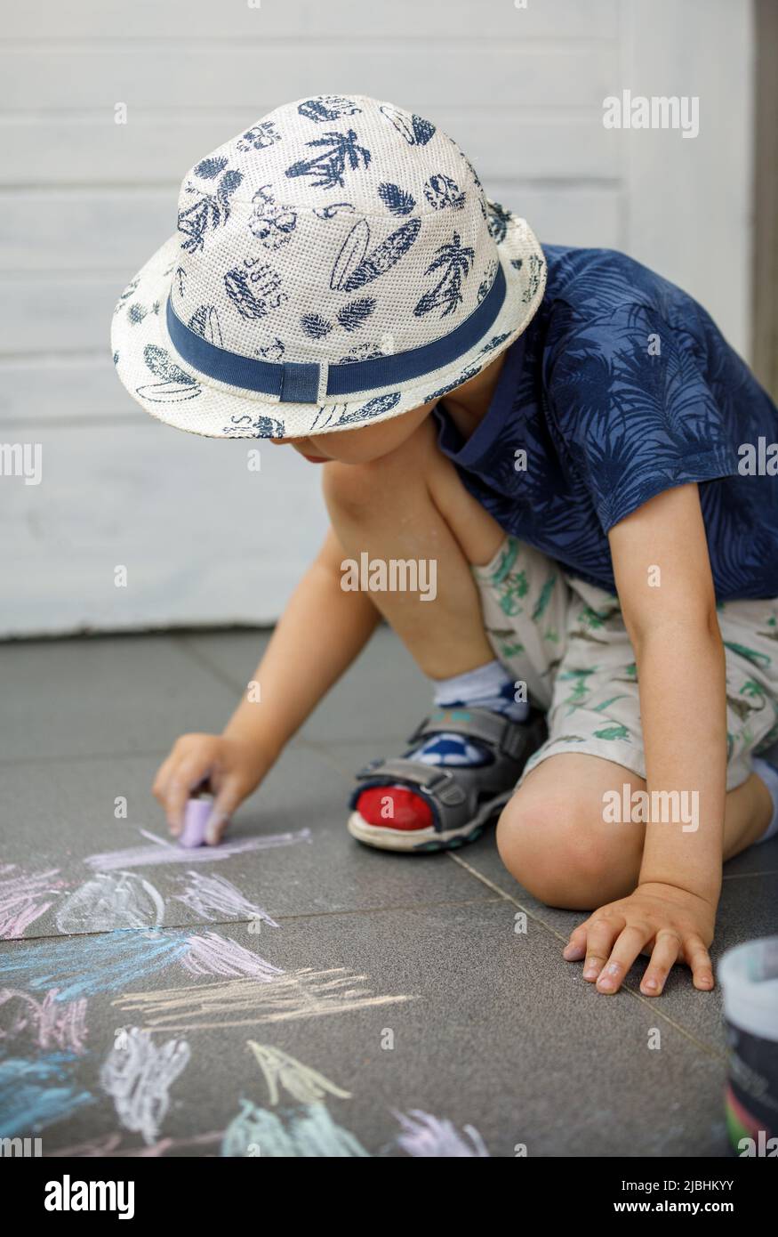 Small caucasian boy three years old sitting on the concrete pavement drawing with chalk in park in day childhood and growing up education concept Stock Photo