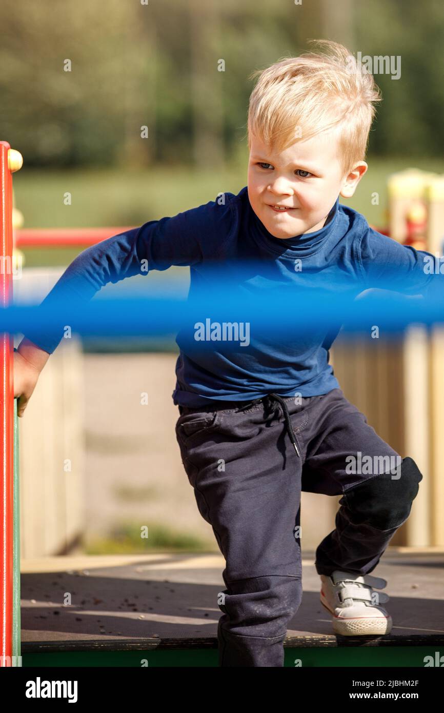 A naughty, very agile boy actively runs through the labyrinths of an outdoor playground. Stock Photo