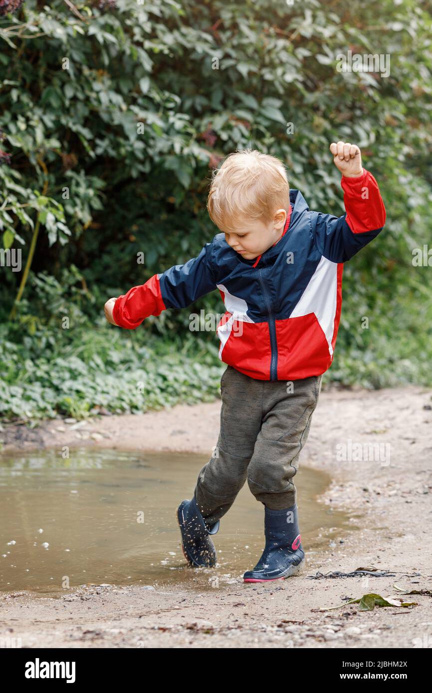 Little boy splashing in a mud puddle, jumping into a puddle. Stock Photo