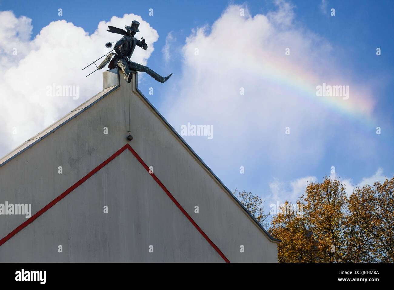 Chimney Sweeper Sculpture on roof in old town of Klaipeda, Lithuania. House wall in Klaipeda Old Town. Blue sky with white clouds and rainbow. Stock Photo