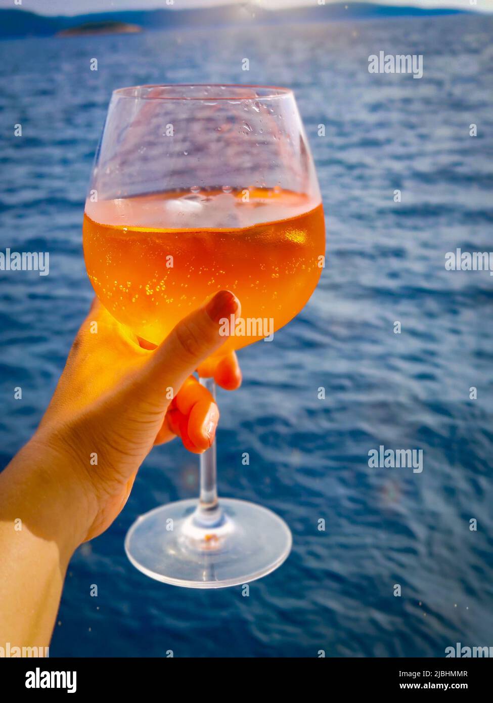 Orange aperol spritz cocktail over the sea on sunset. There is water in the background. Stock Photo