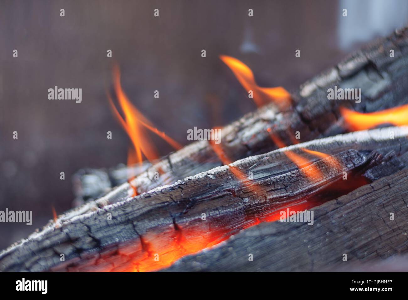 Defocused Firewood is burning in the fireplace in the flames of a warm red fire on a dark background. Briquettes glow and burn, close up Stock Photo