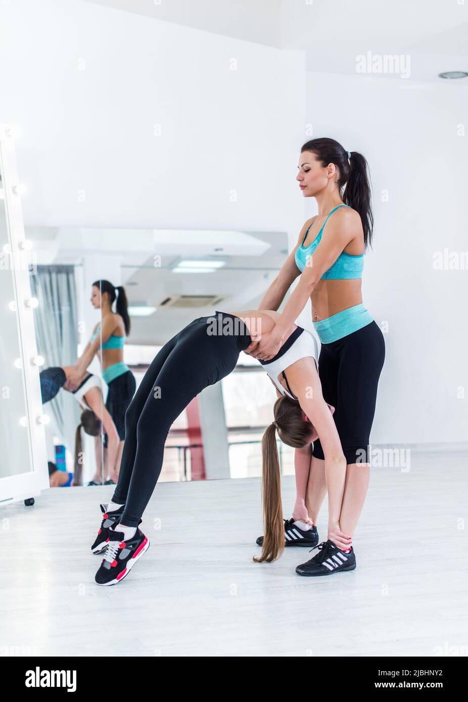 Lithe young Caucasian woman making advanced crab position with the help of personal trainer supporting her back in gym. Stock Photo