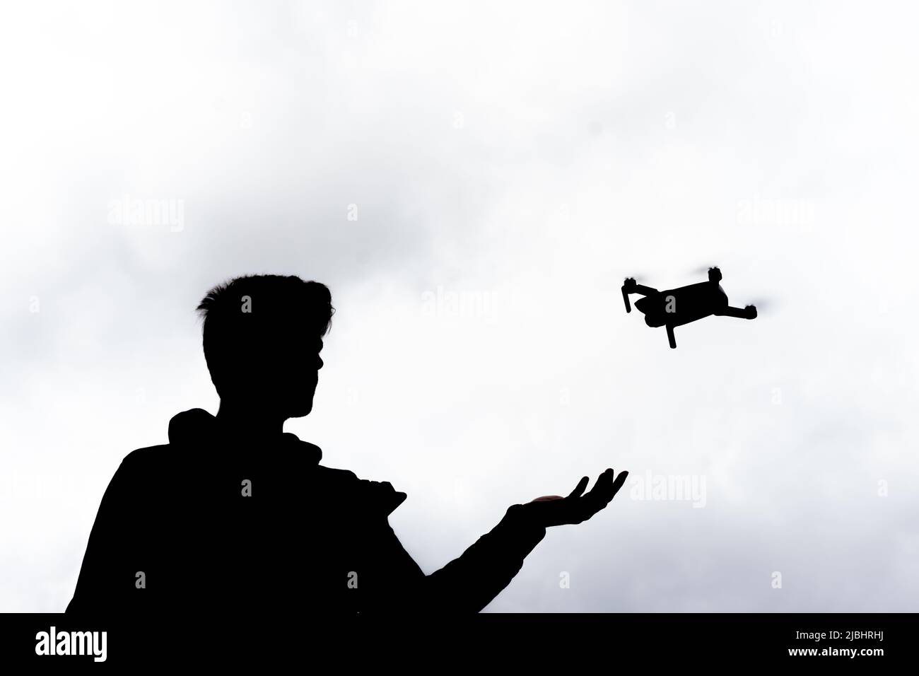 Silhouette of a young man flying a drone outdoor with the sky in background Stock Photo