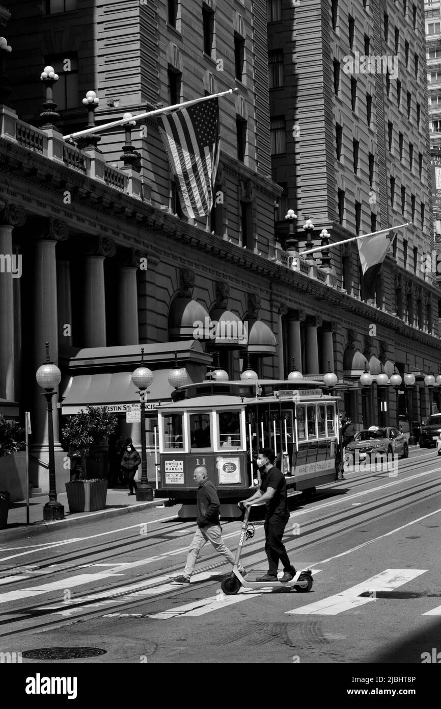 A pedestrian and young man riding an elecric scooter cross a busy street in San Francisco, California. Stock Photo