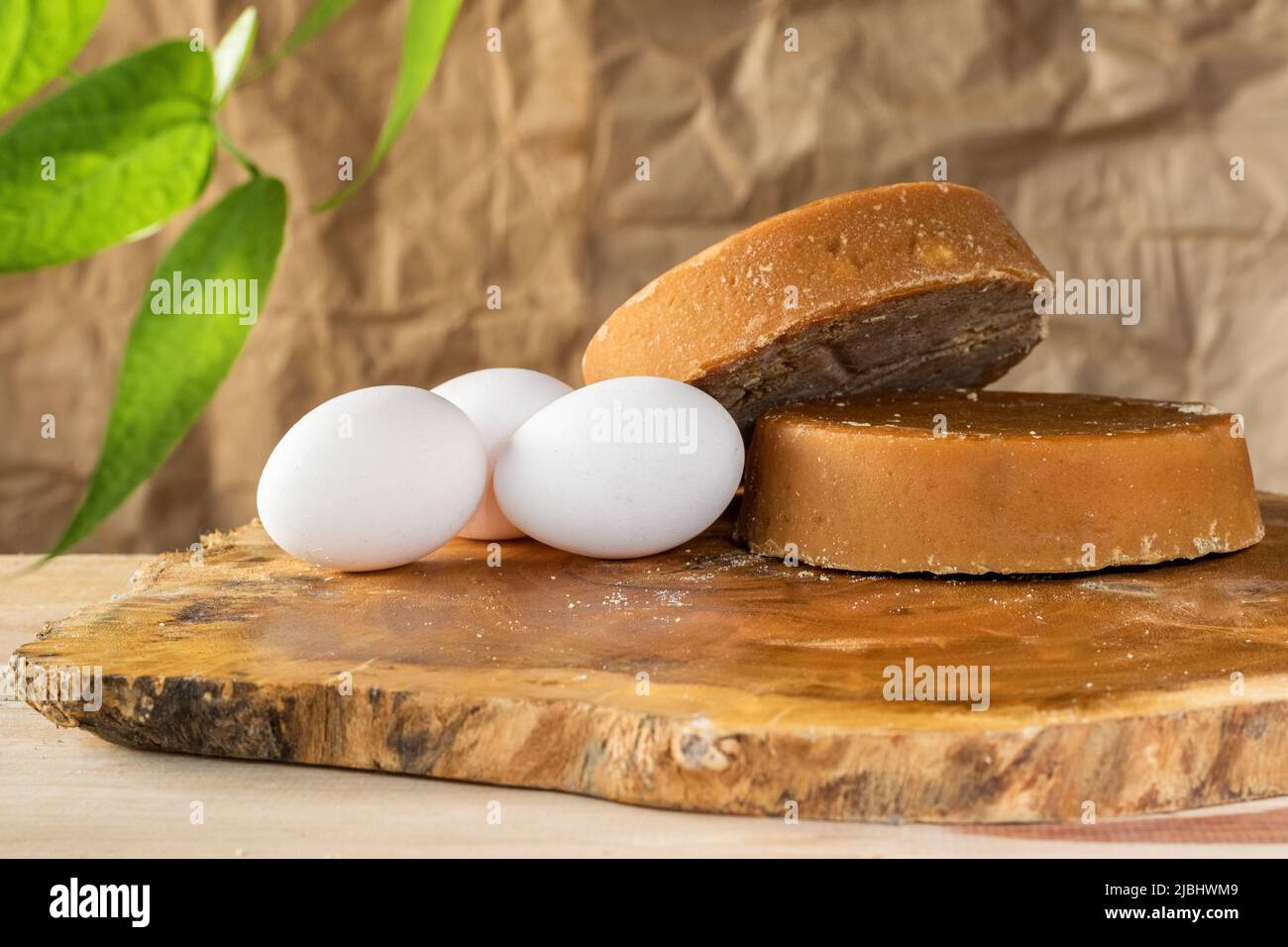 still life of Colombian panela and eggs, placed on a wooden board of cacahuananche (Gliricidia sepium) or Matarraton, with green leaves around them an Stock Photo