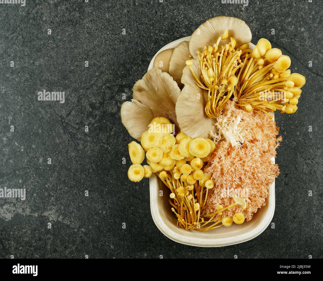 A selection of culinary mushrooms in a punnet from a farmer's market on a black slate kitchen bench top. Stock Photo