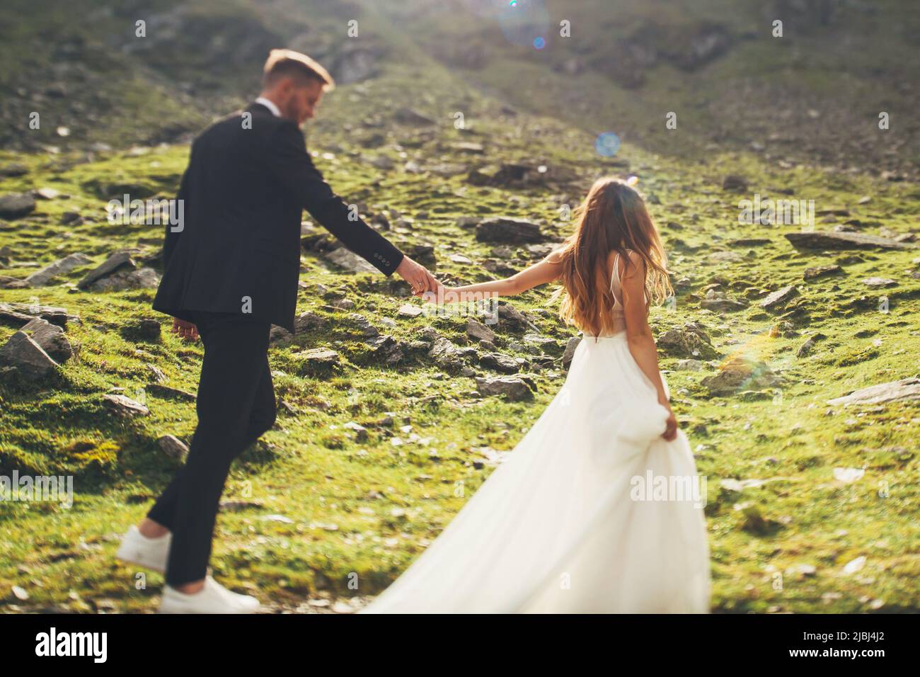 Bride in a dress with lace and groom holding hands and walking during their travel through the mountains. Nature landscape. Stock Photo