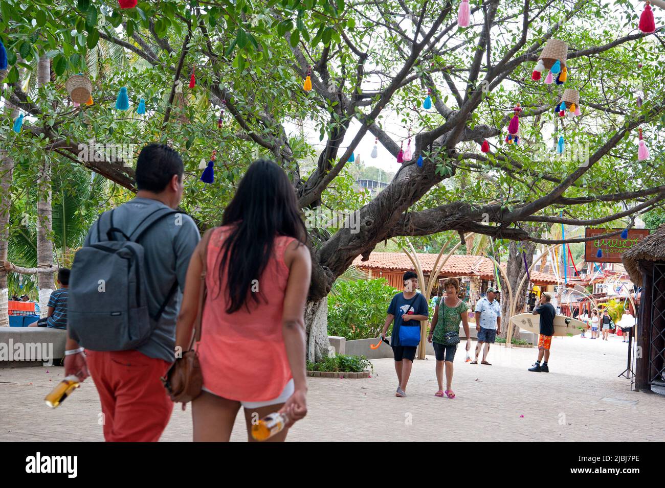 People strolling on tree shaded walkway nearZihuatanejo, Mexico Stock Photo