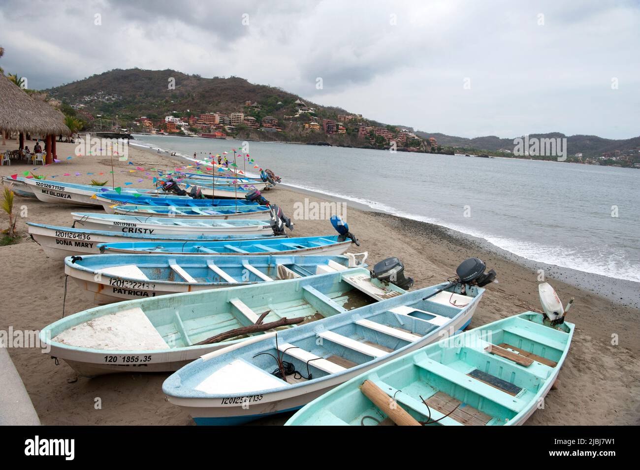 Scenic view of fishing boats on beach with palm trees and hills in Zihuatanejo, Mexico Stock Photo