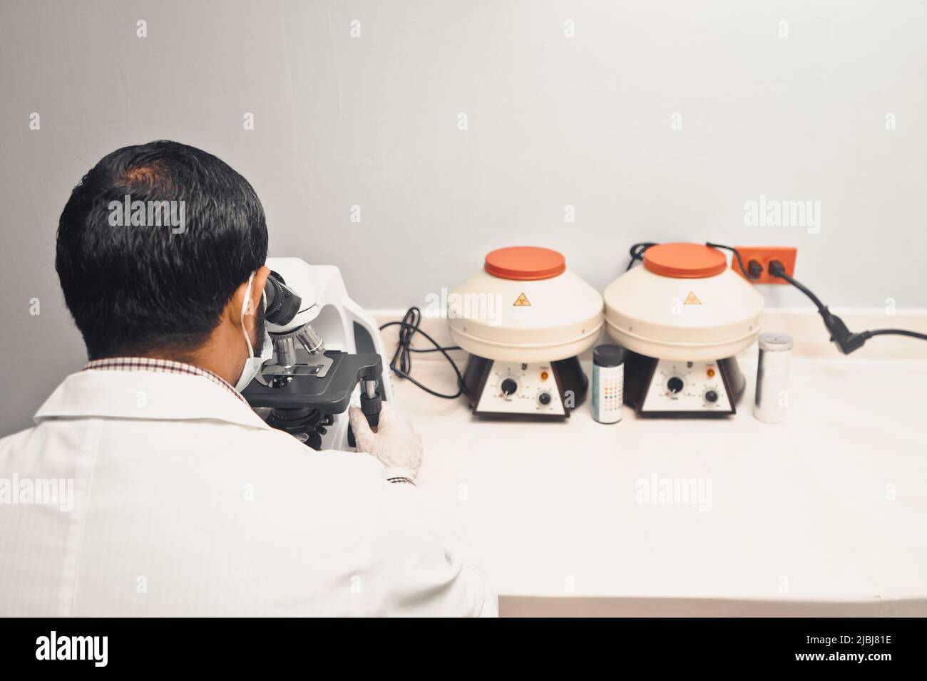 Laboratorian Laboratorian examining a blood sample from behind in a microscope in a ...