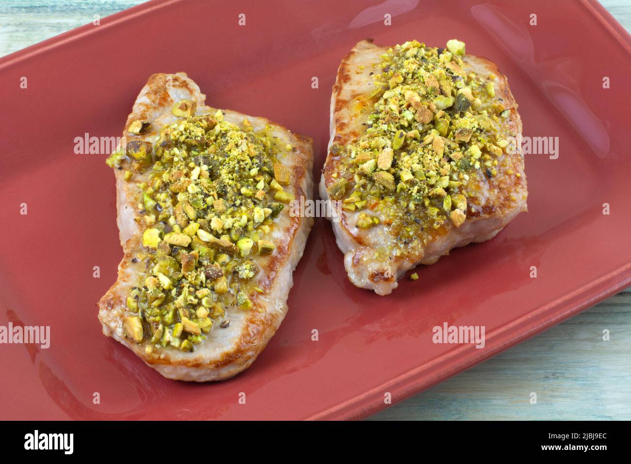 Two boneless pork chops with crushed pistachios on red serving plate Stock Photo