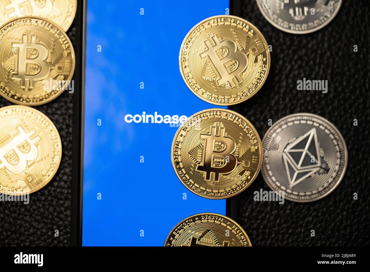Bolzano, Italy - April 10. 2021: Coinbase app running on smartphone next to bitcoin and ethereum coins on Ether surface. Coinbase app to trade crypto Stock Photo