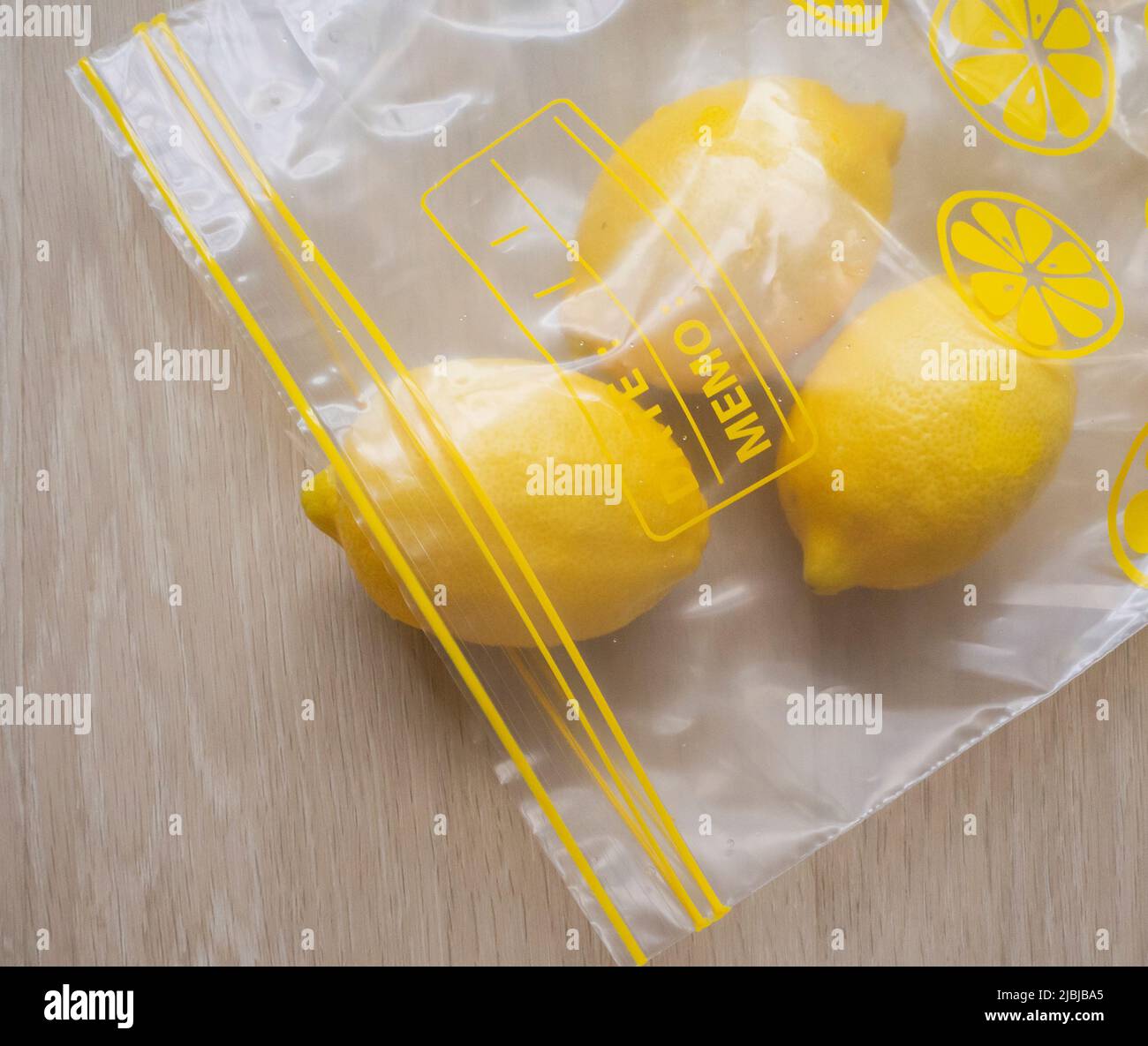 Trio of fresh lemons in a food storage ziplock bag on a light wood