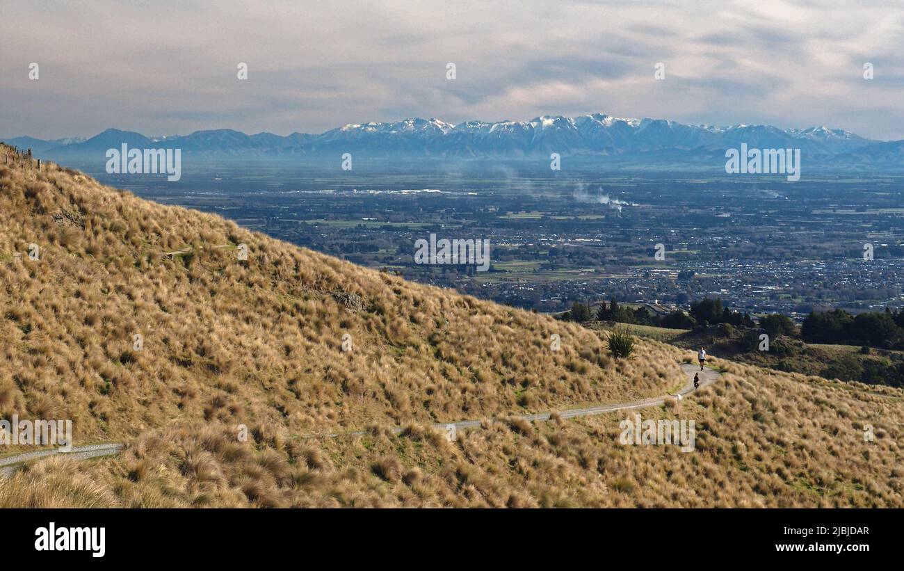 Cyclists riding on a track in the Port Hills Christchurch with a view over the Canterbury Plains to the Southern Alps NZ Stock Photo