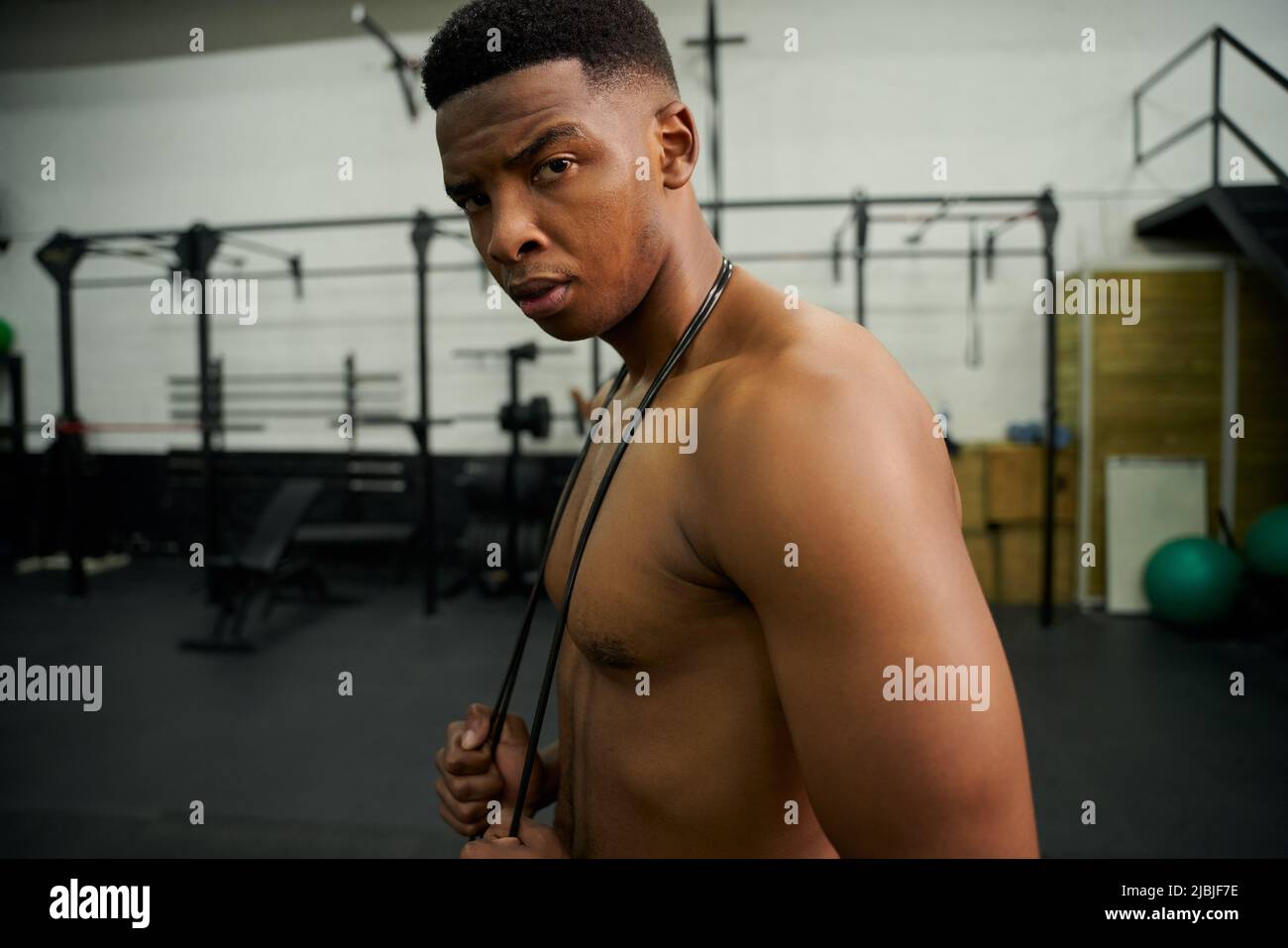 African American male holding skipping rope in the gym. Male athlete looking to the camera during exercise. High quality photo Stock Photo