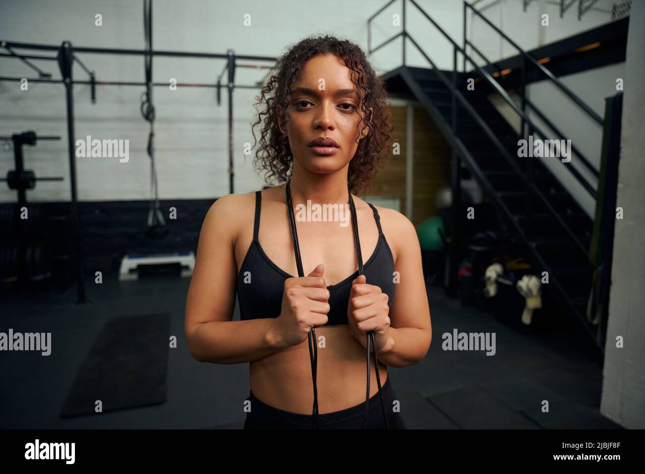 African American female holding skipping rope in the gym. Female athlete looking to the camera during exercise. High quality photo Stock Photo