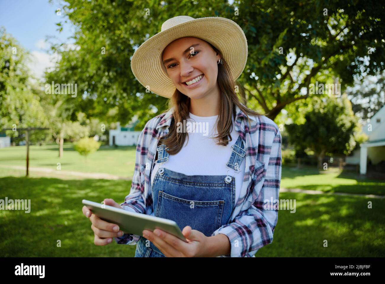 Caucasian female farmer wearing straw hat standing outdoors holding digital tablet  Stock Photo
