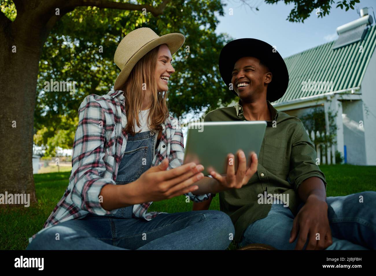 Male and female friends working on farm looking at digital tablet while smiling to eachother Stock Photo