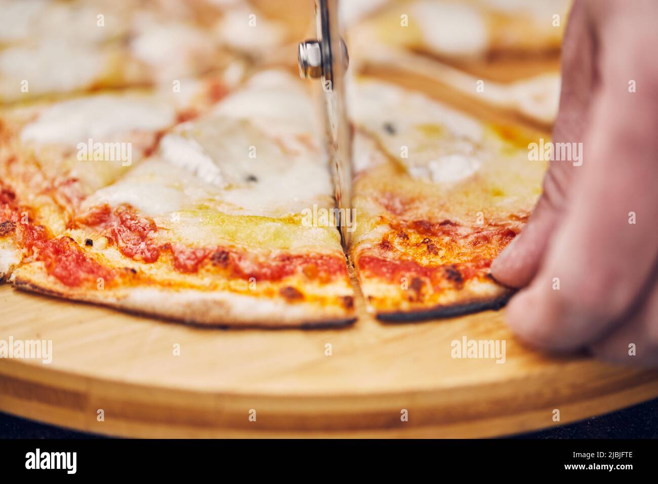 Cutting a pizza with a round pizza cutter. Front view. Stock Photo
