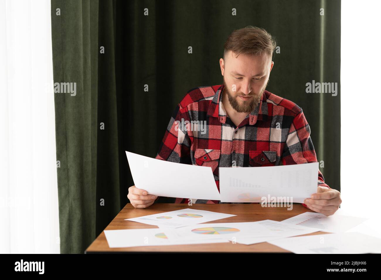 Young businessman working from home, holding a sketch in his hands, working with paper documents, remote analyst analyzes the work of employees Stock Photo