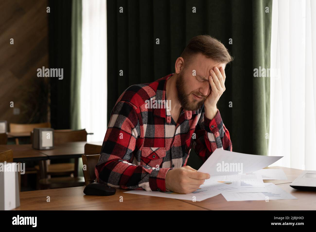 frustrated young man reading documents and using laptop in cafe, money problem, debt notification, bad financial report, money problem, unsuccessful Stock Photo
