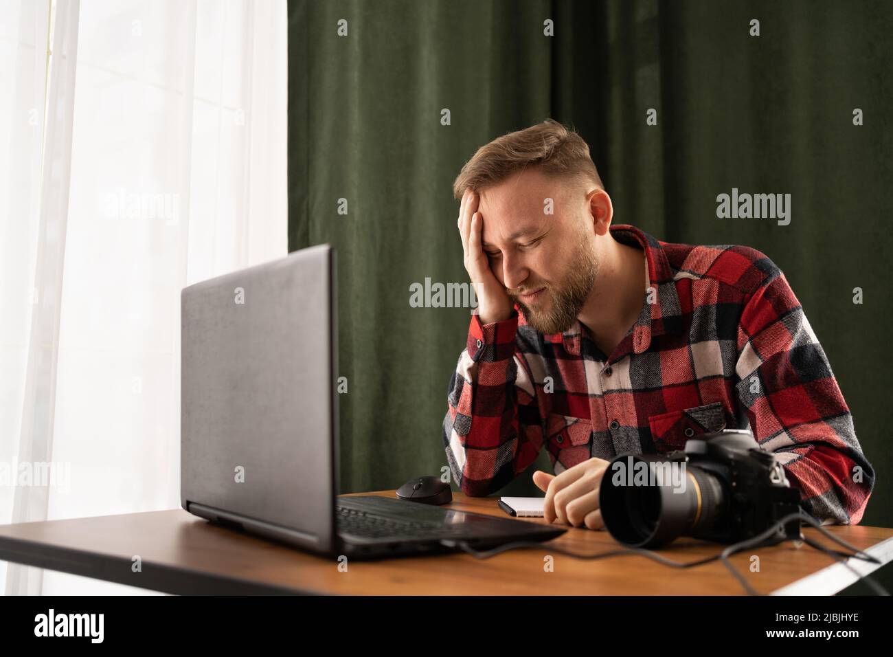 Frustrated Photographer off loading files on laptop. Checking photos working at modern office. editing his images on laptop. problem Stock Photo