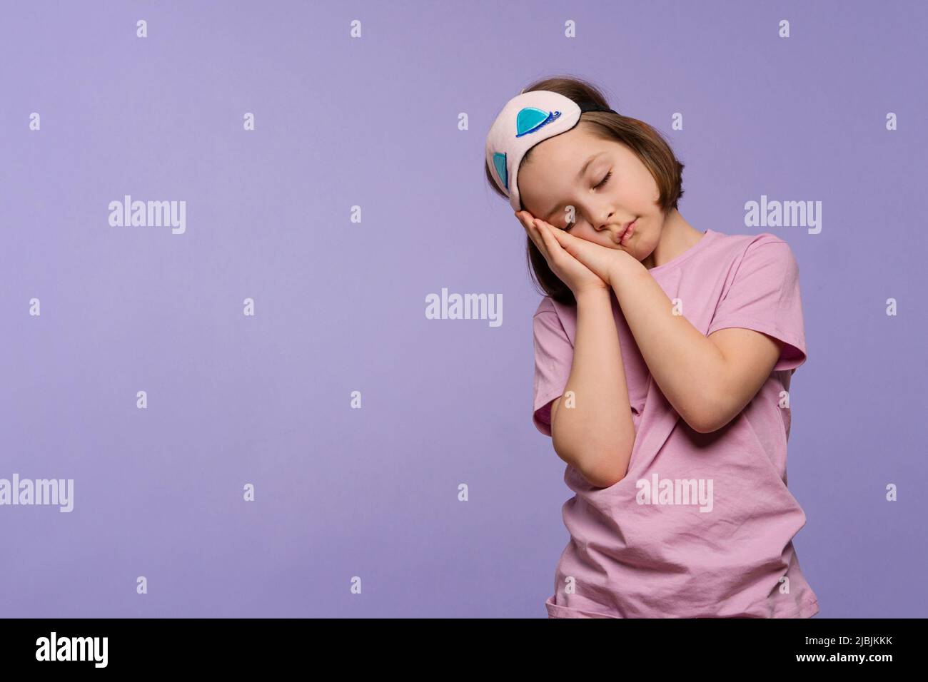 Pretty little girl wearing pink pajamas and sleep mask over lilac