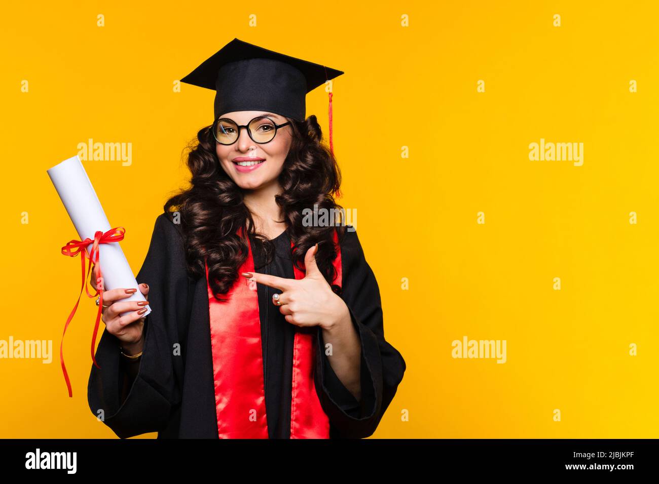 Girl graduate in graduation hat and eyewear with diploma on yellow