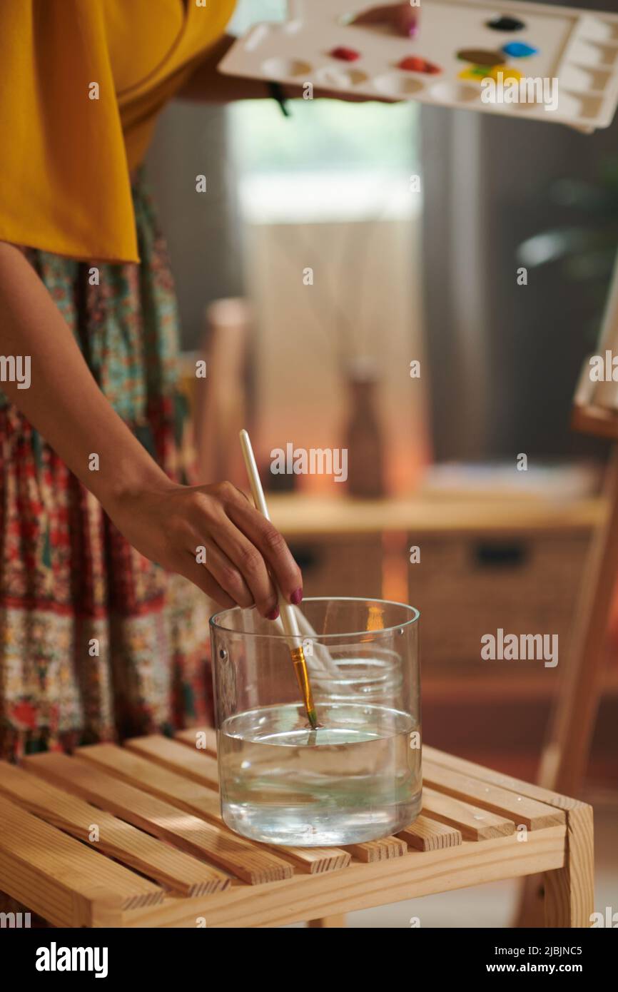 Female painter wetting brush in glass of water before painting Stock