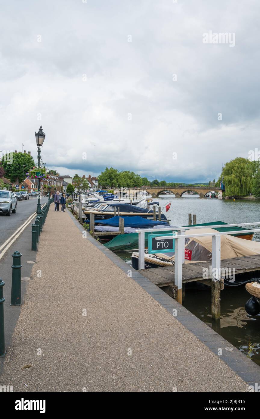View along the river Thames towards Henley Bridge from Thameside footpath. Small leisure craft moored alongside the path. Henley on Thames, England. Stock Photo