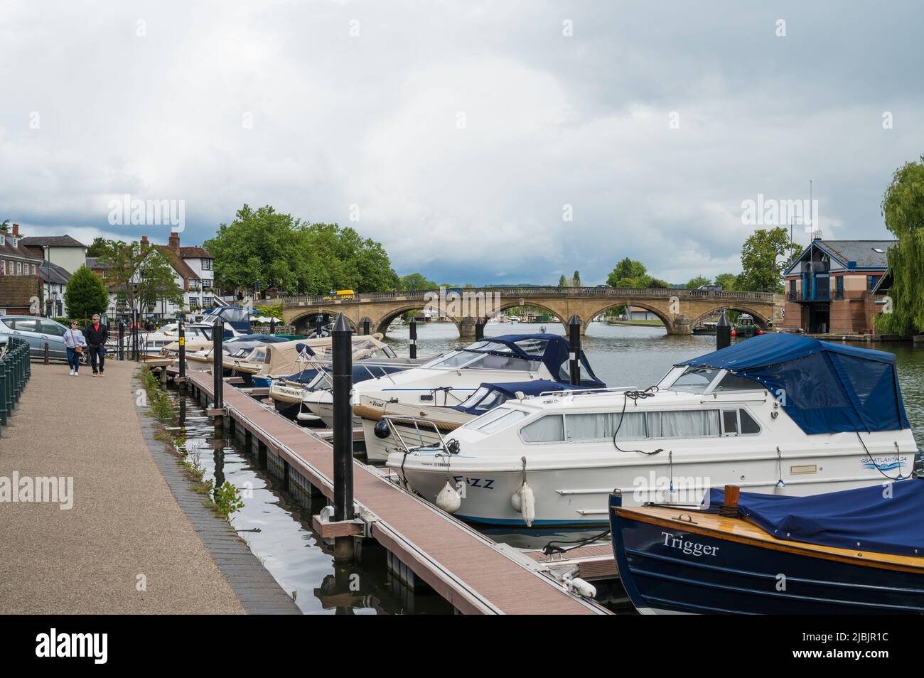 View along the river Thames towards Henley Bridge from Thameside footpath. Small leisure craft moored alongside the path. Henley on Thames, England. Stock Photo