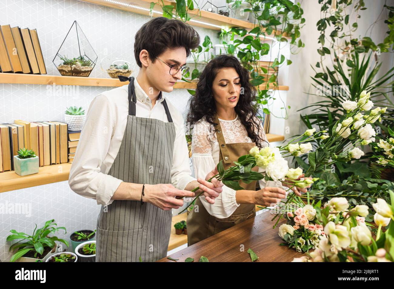 Attractive experienced female florist teaches a young man how to work in a flower shop Stock