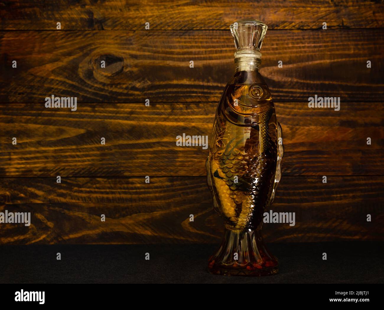 Bottle of alcohol in the form of a fish with a snake inside on a dark wooden background. Traditional Asian liquor. A snake in a bottle Stock Photo