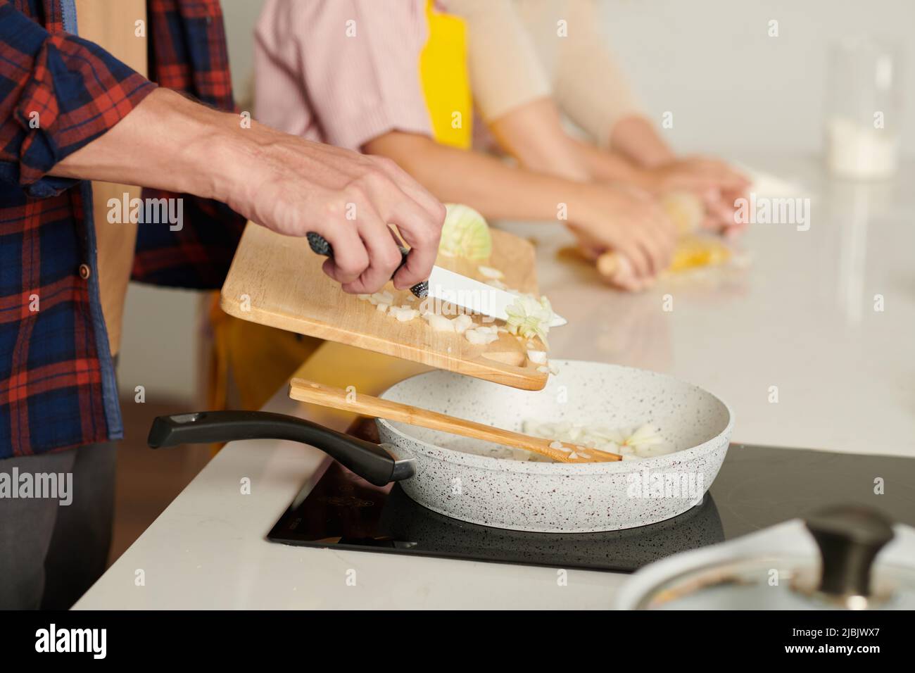 Hands of man adding chopped onion in hot saucepan with cooking oil ...