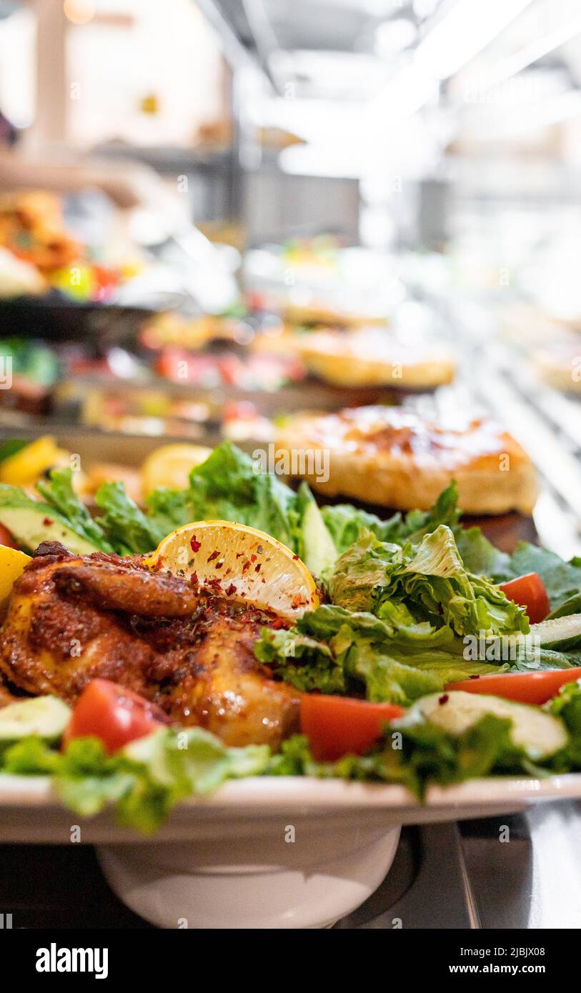 Tobacco chicken with lemon and tomato among other out-of-focus dinner food. Selective focus, vertical copy space Stock Photo